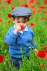 Little boy standing in field and smelling poppy — Stock Photo