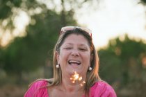 Portrait of a happy middle aged woman holding sparkler and laughing — Stock Photo