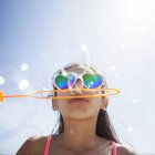 Girl in heart shaped sunglasses on beach blowing bubbles with bubble wand — Stock Photo