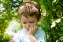 Хлопчик стоїть в саду з рукою на підборідді — стокове фото