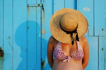 Вагітна жінка в солом'яному капелюсі стоїть перед синьою стіною — стокове фото