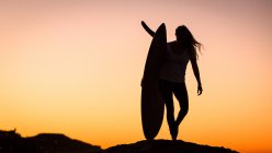 Silhouette of woman carrying surfboard at sunset — Stock Photo