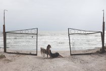 Вид збоку молодої жінки, що сидить на піщаному пляжі з собакою — стокове фото