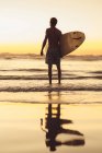 Homme debout sur la plage au lever du soleil tenant planche de surf, San Diego, Californie, Amérique, États-Unis — Photo de stock