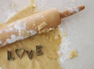 Pâte, rouleau à pâtisserie et découpeuses orthographe mot amour — Photo de stock
