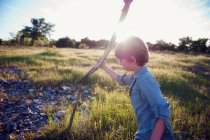 Мальчик держит деревянную палку в природе — стоковое фото