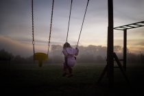 Girl sitting on swing in morning fog — Stock Photo