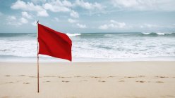 Bandera roja ondeando en el viento en la playa de arena - foto de stock