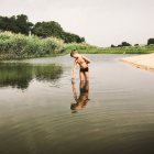Niño de pie y tocando el agua en el río en verano - foto de stock