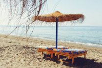 Живописный вид на соломенный зонтик и два шезлонга на пляже — стоковое фото