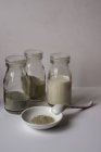 Tre bottiglie con polvere e latte contro parete grigia — Foto stock