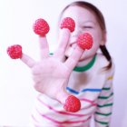 Primo piano di ragazza che mostra lamponi sulle dita — Foto stock