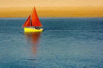 Yellow sailboat with red sails by beach — Stock Photo