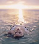 Jeune femme flottant en mer au coucher du soleil — Photo de stock