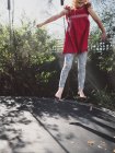 Дівчина стрибає на батуті в саду з розтягнутими руками — стокове фото