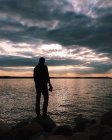Silhouette dell'uomo in piedi su roccia in spiaggia e tenendo una macchina fotografica — Foto stock