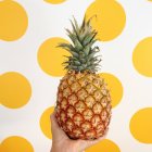 Female hand holding pineapple in front of yellow spot background — Stock Photo
