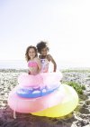 Duas meninas bonitos se divertindo com anéis de flutuação na praia — Fotografia de Stock