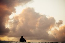Silueta de surfista esperando para coger una ola bajo el cielo nublado - foto de stock