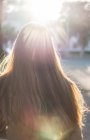 Rückansicht einer Frau mit langen Haaren, die im Sonnenlicht die Straße entlang läuft — Stockfoto