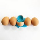Fila de ovos com uma tinta aberta e azul rachada derramando — Fotografia de Stock