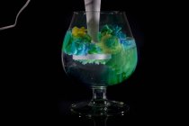 Yellow and blue acrylic paint blended in glass of water — Stock Photo