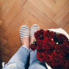 Pernas femininas e flores vermelhas frescas no saco no chão de madeira — Fotografia de Stock