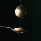 Dripping oil from one spoon onto another against black background — Stock Photo