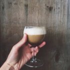 Cropped image of female hand holding glass of irish coffee drink — Stock Photo