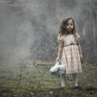 Girl wearing dress standing in woods and holding a teddy bear — Stock Photo