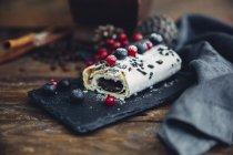 Tempting chocolate roll with summer fruits and icing sugar on gentrice black stone slab, heritage style — Stock Photo
