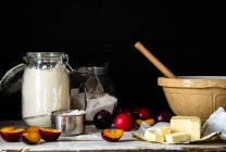Baking ingredients for a plum cake in kitchen against black background — Stock Photo
