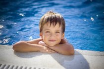 Retrato del niño sonriente apoyado en el borde de una piscina - foto de stock