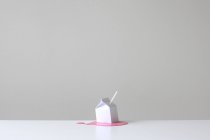 Cartón de leche blanca conceptual con paja blanca en un charco de leche de fresa rosa - foto de stock