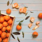 Fresh sweet tangerines in basket and on wooden surface with leaves — Stock Photo