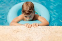 Ritratto di ragazzo che galleggia in un anello di gomma in una piscina aggrappata al bordo della piscina — Foto stock