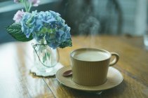Xícara de café ao lado de um vaso de hortênsias — Fotografia de Stock