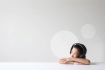 Мальчик в наушниках слушает музыку за белым столом — стоковое фото