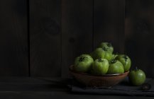 Green tomatoes in bowl on table against dark background — Stock Photo