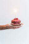 Mão masculina segurando um bolo de aniversário de esponja victoria com uma vela — Fotografia de Stock
