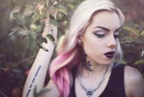 Портрет молодой женщины с татуировками, стоящей в саду — стоковое фото