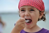 Крупным планом маленькая девочка в бандане ест мороженое — стоковое фото
