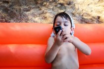 Niño pequeño acostado en la balsa de la piscina roja usando el teléfono móvil - foto de stock