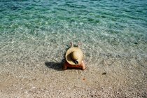 Woman with straw hat sunbathing in water on beach — Stock Photo