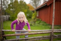 Fille escalade sur la clôture en bois à l'extérieur de la maison suédoise traditionnelle — Photo de stock