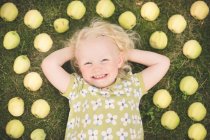 Petite fille blonde allongée sur l'herbe entourée de pommes — Photo de stock