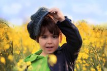 Boy putting on cap in yellow rape seed field — Stock Photo