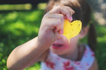 Girl holding a heart shaped leaf in front of her face — Stock Photo