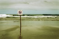 Spiaggia deserta con cartello che proibisce il nuoto — Foto stock