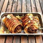 Tasty roasted porchetta in baking tray over wooden table — Stock Photo